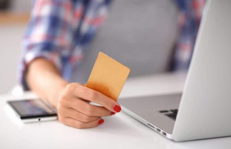 Woman online shopping using computer and credit card in kitchen